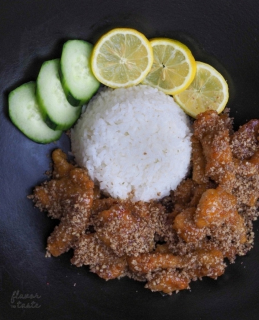 Crushed pecan-dusted glazed chicken plated on a black dish with rice and garnish