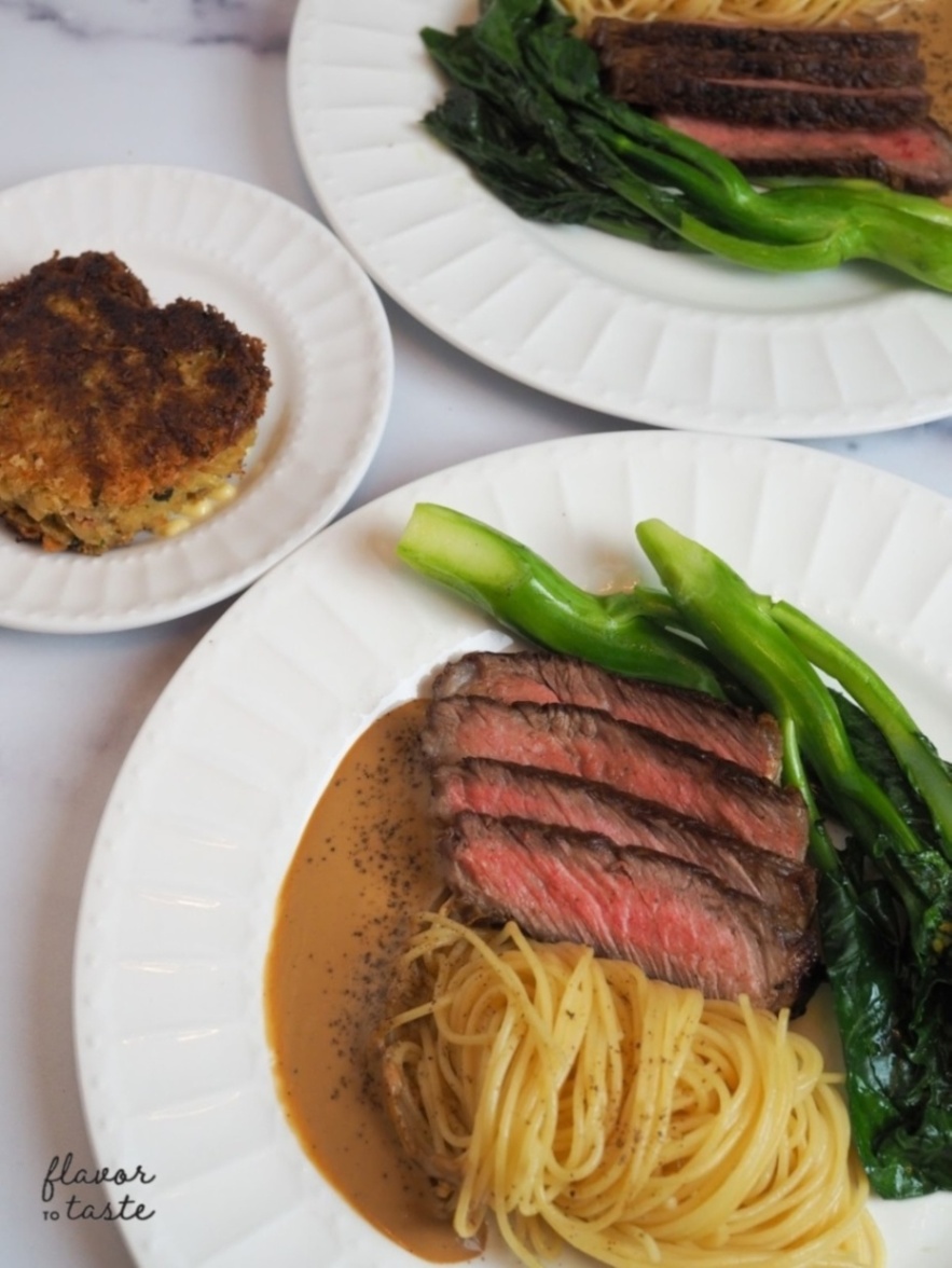 Sliced ribeye plated with black pepper sauce-topped spaghetti and greens